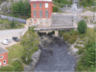 Foto de uma pequena central hidrelétrica de High Falls. Uma estrutura de galpão com tijolos e janelas, e embaixo da estrutura três passagens de água.