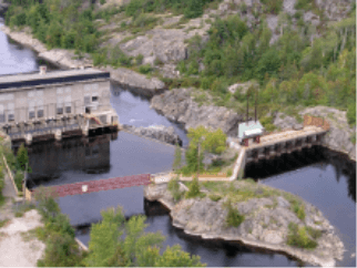 Photo of Wabageshik small hydropower plant with a concrete structure, rocks, vegetation, and moving water passing through the structures.