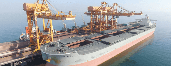 Large cargo ship docked at the Sohar port. Next to it are about three pieces of crane-like equipment