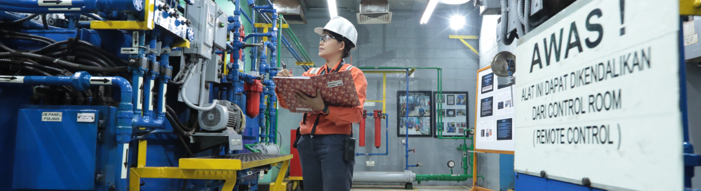A Vale employee holds a notebook as she walks through the machine area. She is wearing a helmet and goggles