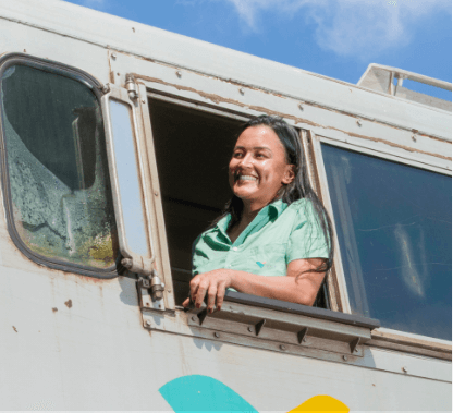 Mulher sorrindo na direção de um dos trens da Vale. Ela está usando uma camisa verde clara.