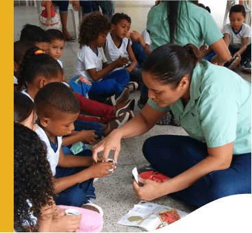 Diversas crianças estão sentadas no chão, interagindo com duas empregadas Vale.