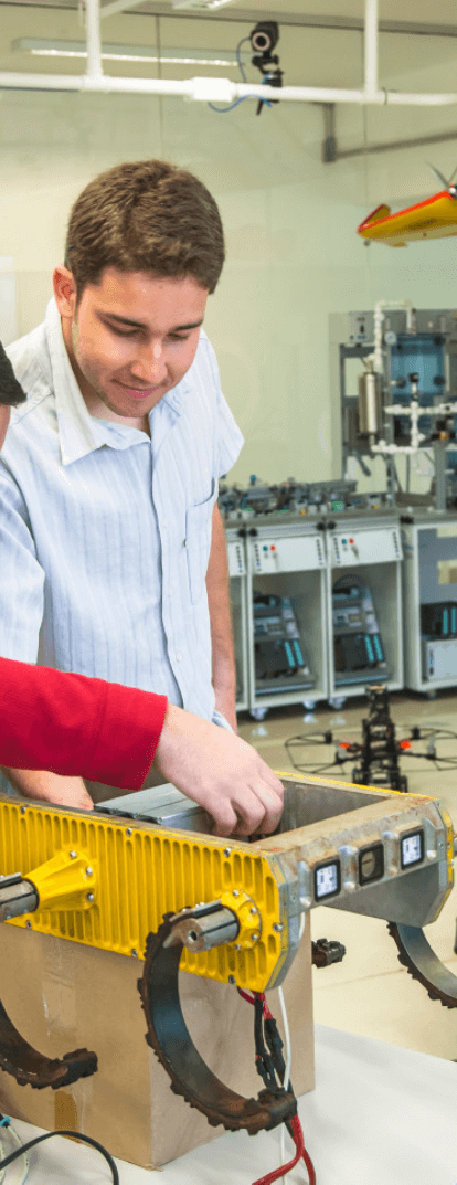 Two young men are working on iron equipment. Both are standing and smiling.