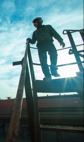 A man going down the stairs in an operations space. He is against the sun and the photo is shaded. In the background, there is a blue sky.