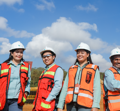 A group of Vale employees in an open area. They are wearing vests, uniforms and protective hats.