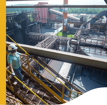 Imagem de uma empregada Vale, de capacete e luvas de proteção, descendo escadas em meio a uma operação. O local tem diversos equipamentos de metal.