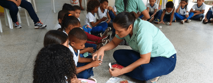 Diversas crianças estão sentadas no chão, interagindo com duas empregadas Vale.