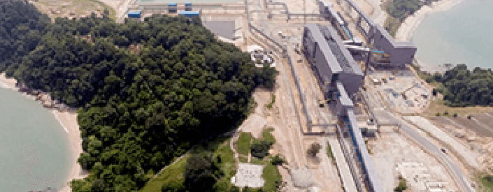 Aerial image of Teluk Rubiah Terminal. On the left is an area of vegetation, underneath you can see water, and in the rest of the image is an operation area with large equipment.