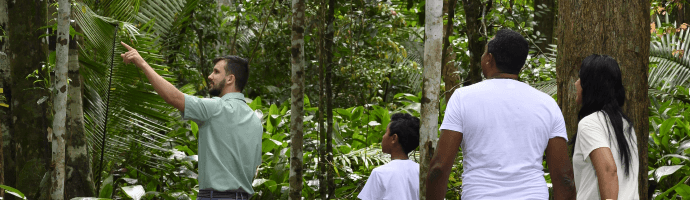 Um empregado está acompanhado de outras pessoas por uma trilha em um local bastante arborizado.