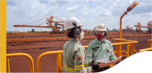 Dois empregados Vale estão em uma área de operação externa. Ambos usam equipamentos de proteção.