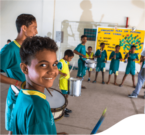 Several children gathered playing musical instruments in a court. They are all wearing green clothes and a boy looks at the camera smiling.