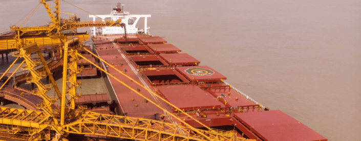 Image of the top of a large cargo ship, with yellow equipment operating. In the background the waters are murky.