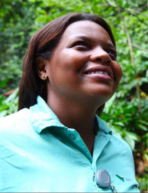Chest to head shot of a black woman looking upwards and smiling, wearing a green Vale uniform, green button-up shirt